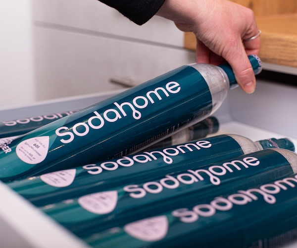 Sodahome-CO2-Zylinder-Schublade-Produkt Eine Hand greift nach einem Sodahome CO₂-Zylinder aus einer Schublade, in der mehrere Zylinder ordentlich gelagert sind.