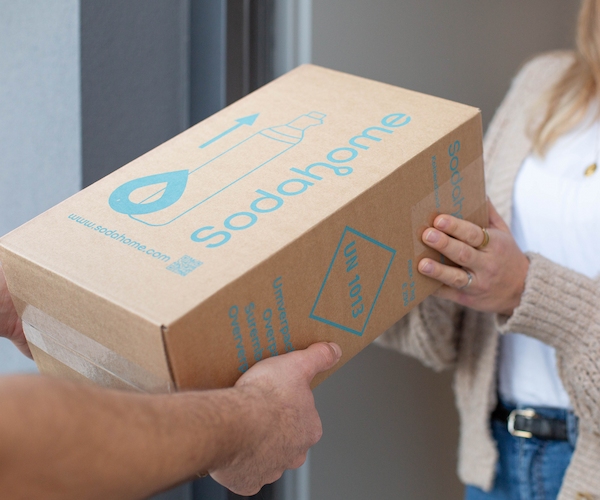 Sodahome-Lieferservice-CO2-Zylinder Übergabe eines Sodahome-Pakets an der Haustür, das umweltfreundlich verpackte CO₂-Zylinder für Wassersprudler enthält.
