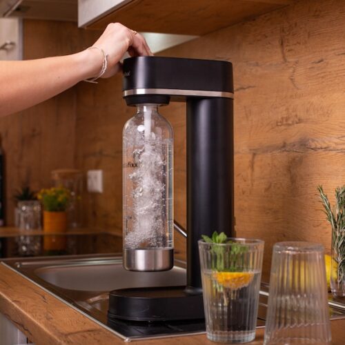 Eine Frau benutzt den Sodafixx Wassersprudler in einer modernen Küche. Im Sprudler befindet sich eine Sodafixx PET Flasche